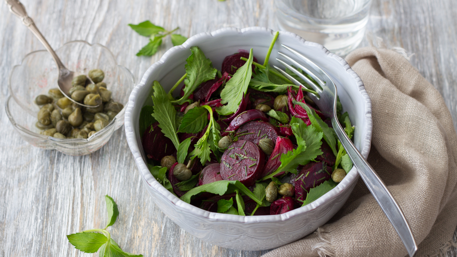 Bowl of beetroot and green leaf salad with pickled wild allium capers on the side