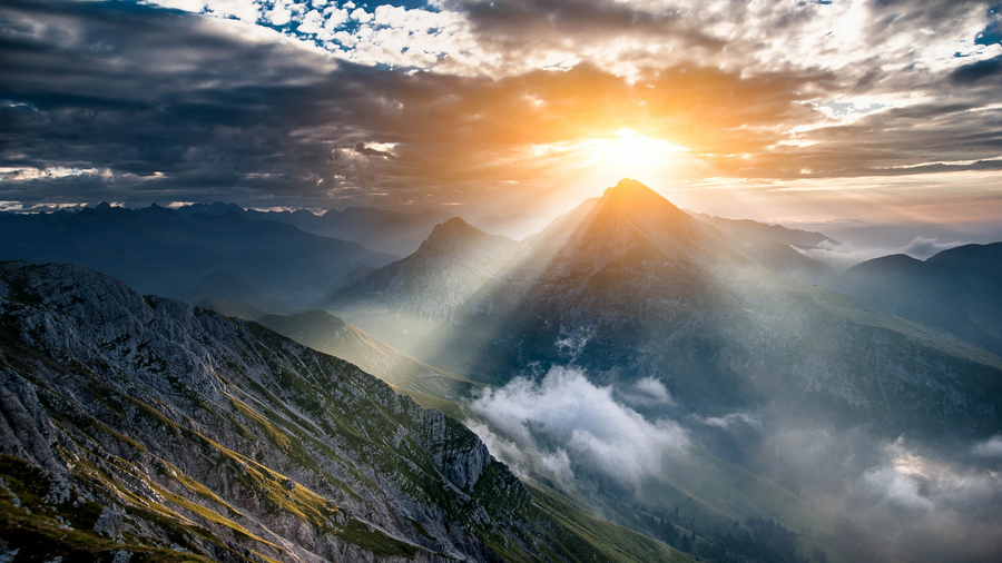 Sun breaking through clouds over a mountain range